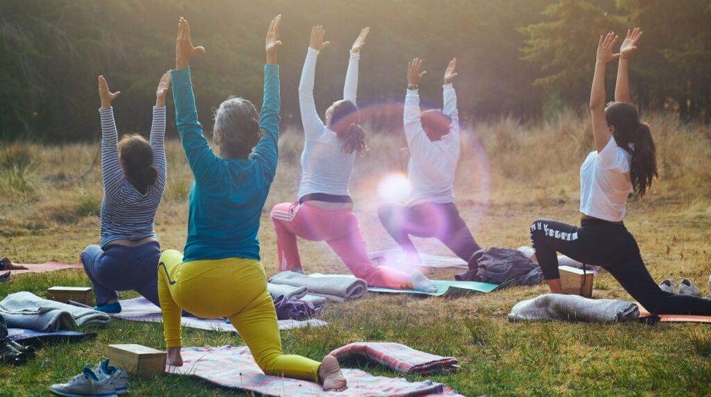 En grupp på fem personer som gör yoga på ett fält